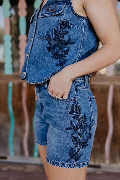 Person wearing a denim outfit with floral embroidery in an outdoor setting